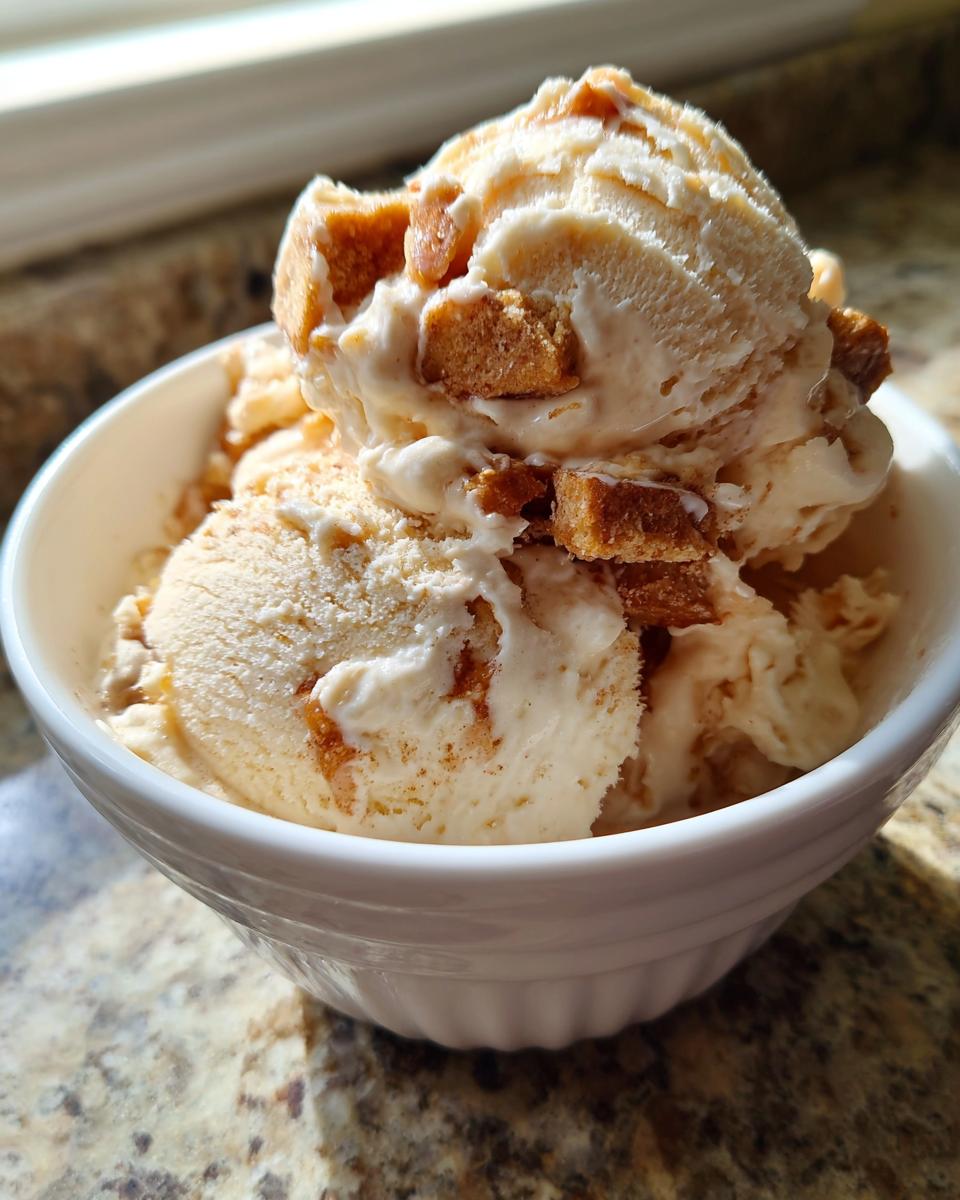Two scoops of creamy apple pie ice cream loaded with chunks of pie crust topping in a white bowl.
