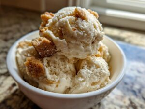 Close-up of scoops of creamy apple pie ice cream topped with brown sugar crumble pieces in a white bowl.
