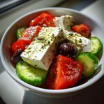 A vibrant bowl featuring chunks of feta cheese, tomatoes, cucumbers, and Kalamata olives, seasoned for a perfect greek salad.