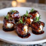 Close-up of five glazed, bacon-wrapped stuffed dates filled with white cheese and topped with rosemary.
