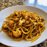 A close-up of black pepper turmeric cauliflower and garlic noodles tossed in a yellow sauce, served in a white bowl.