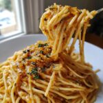 A fork lifting a generous portion of creamy caramelized onion pasta, garnished with fresh thyme.