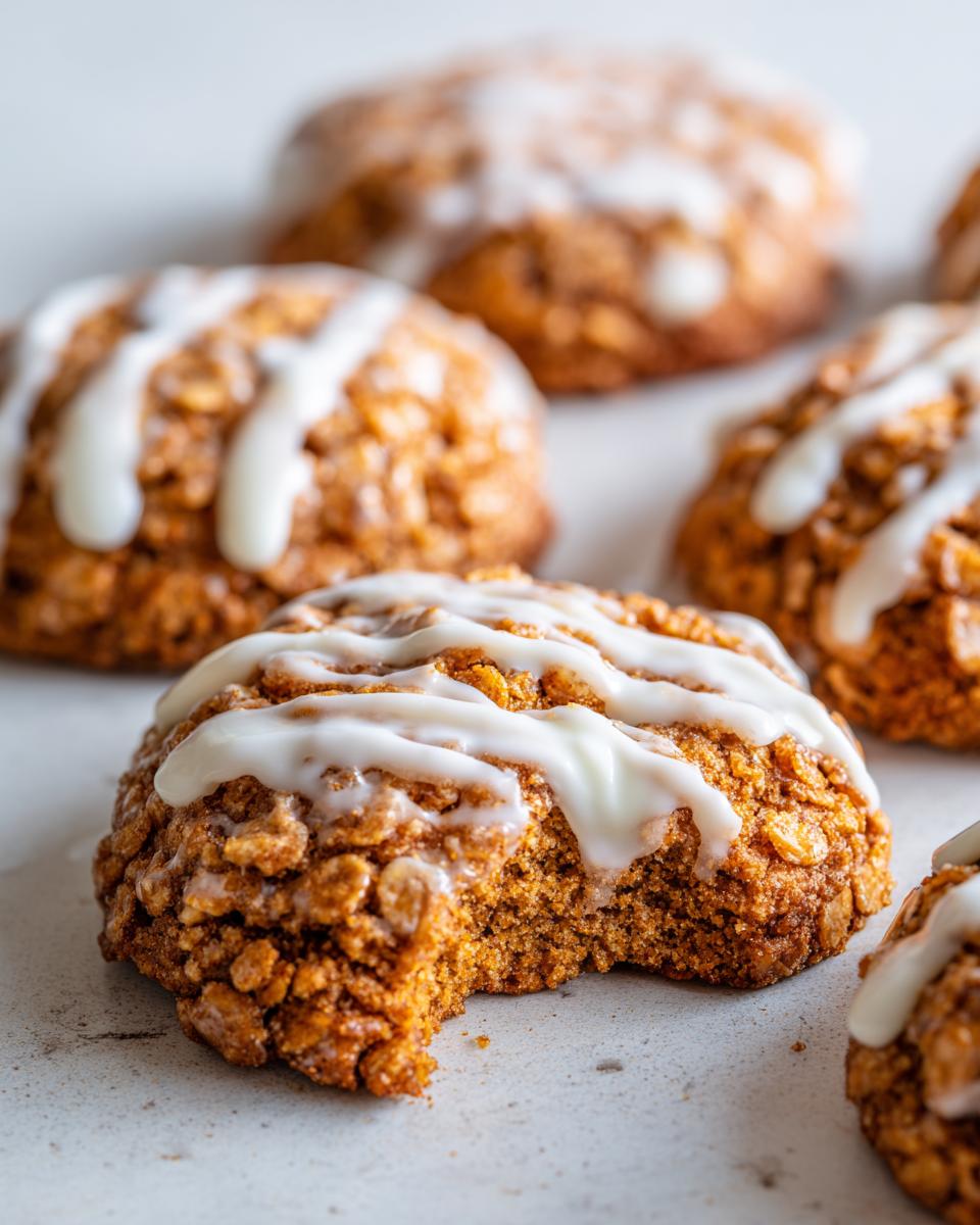 A close-up of a soft, orange-brown cinnamon toast crunch cookie with a bite taken out, drizzled with white vanilla icing.