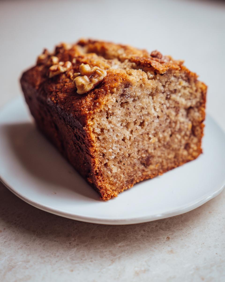 A moist slice of cottage cheese banana bread topped with walnuts, served on a white plate.