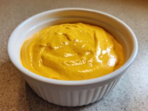Close-up of vibrant, smooth cottage cheese queso dip served in a small white fluted bowl.