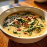 A close-up of a creamy bean soup bowl topped with wilted spinach, crumbled sausage, and black pepper.