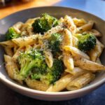 Close-up of a bowl filled with creamy broccoli pasta, penne noodles coated in sauce and topped with grated cheese.
