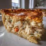 A close-up cross-section of a rich chicken pot pie slice showing shredded chicken, vegetables, and creamy sauce under a golden flaky crust.