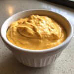 A close-up of thick, vibrant orange cottage cheese queso served in a small white fluted ramekin.
