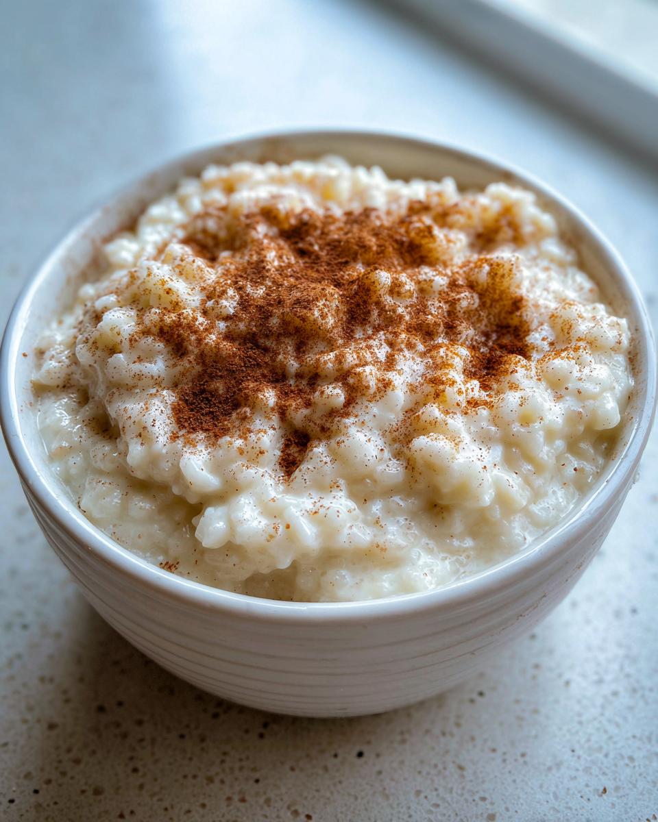 Close-up of a white bowl filled with creamy rice pudding, generously dusted with ground cinnamon.
