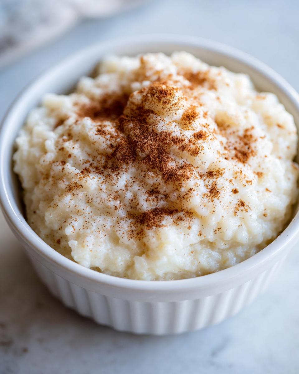 Close-up of creamy rice pudding in a white ramekin, generously topped with ground cinnamon.