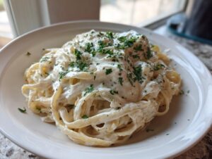 A close-up of fettuccine pasta generously coated in creamy vegan alfredo sauce and topped with fresh parsley.