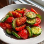 Close-up of fresh cucumber tomato salad tossed in herbs and dressing in a white bowl.