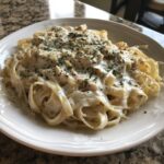 A plate of fettuccine pasta generously coated in a rich, creamy vegan alfredo sauce and topped with herbs.