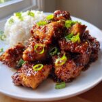 Close-up of sticky, glazed honey garlic chicken pieces served next to a mound of white rice and topped with green onions.