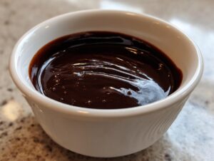 Close-up of smooth, dark, glossy chocolate ganache in a small white bowl.