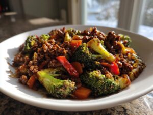 A close-up of a serving of glossy ground beef stir fry mixed with bright green broccoli florets and red bell peppers.