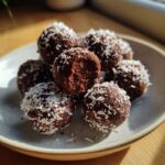 A pile of rich, dark high protein coffee truffles rolled in shredded coconut flakes on a light plate.