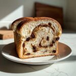 A thick slice of homemade raisin bread showing a beautiful cinnamon swirl and plump raisins throughout the soft crumb.