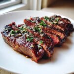 Perfectly cooked and sliced air fryer steak, glistening with juices and topped with minced garlic and parsley.