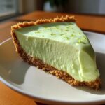A perfect slice of creamy, light green key lime cheesecake with a graham cracker crust, topped with lime zest.