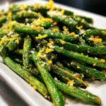 A close-up of bright green, roasted green beans topped with grated parmesan cheese and vibrant lemon zest, ready to serve.