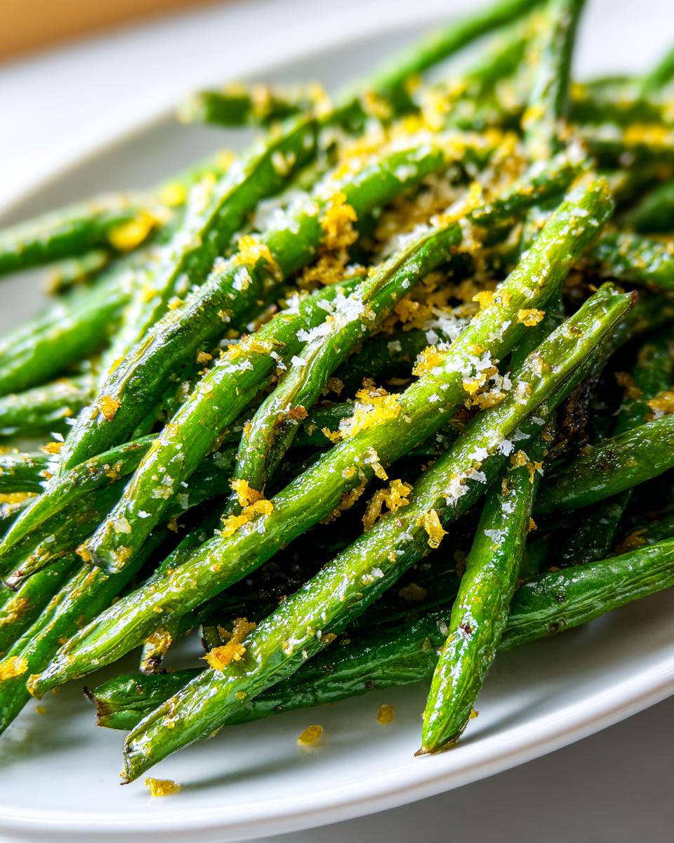 Close-up of bright green, roasted green beans topped with grated parmesan and lemon zest, ready to serve.