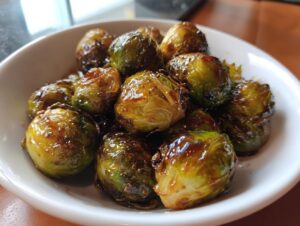 Close-up of perfectly caramelized miso-honey roasted brussels sprouts glistening with glaze in a white bowl.