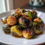 A close-up of perfectly caramelized miso-honey roasted brussels sprouts piled on a white plate.