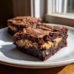 A close-up of a rich, fudgy peanut butter stuffed brownies square sitting on a light plate, showing the creamy filling.