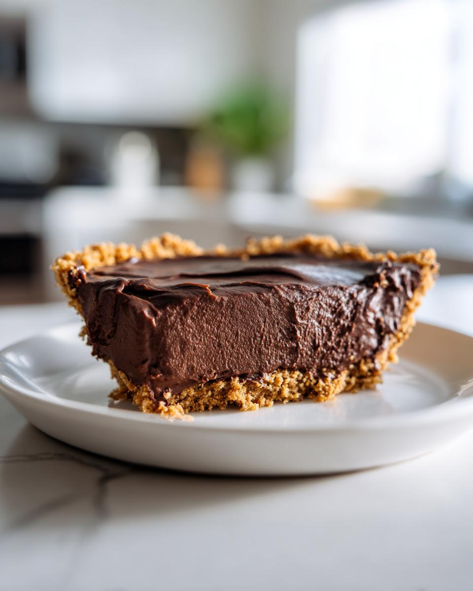 Close-up of a thick slice of rich chocolate pie with a graham cracker crust served on a white plate.