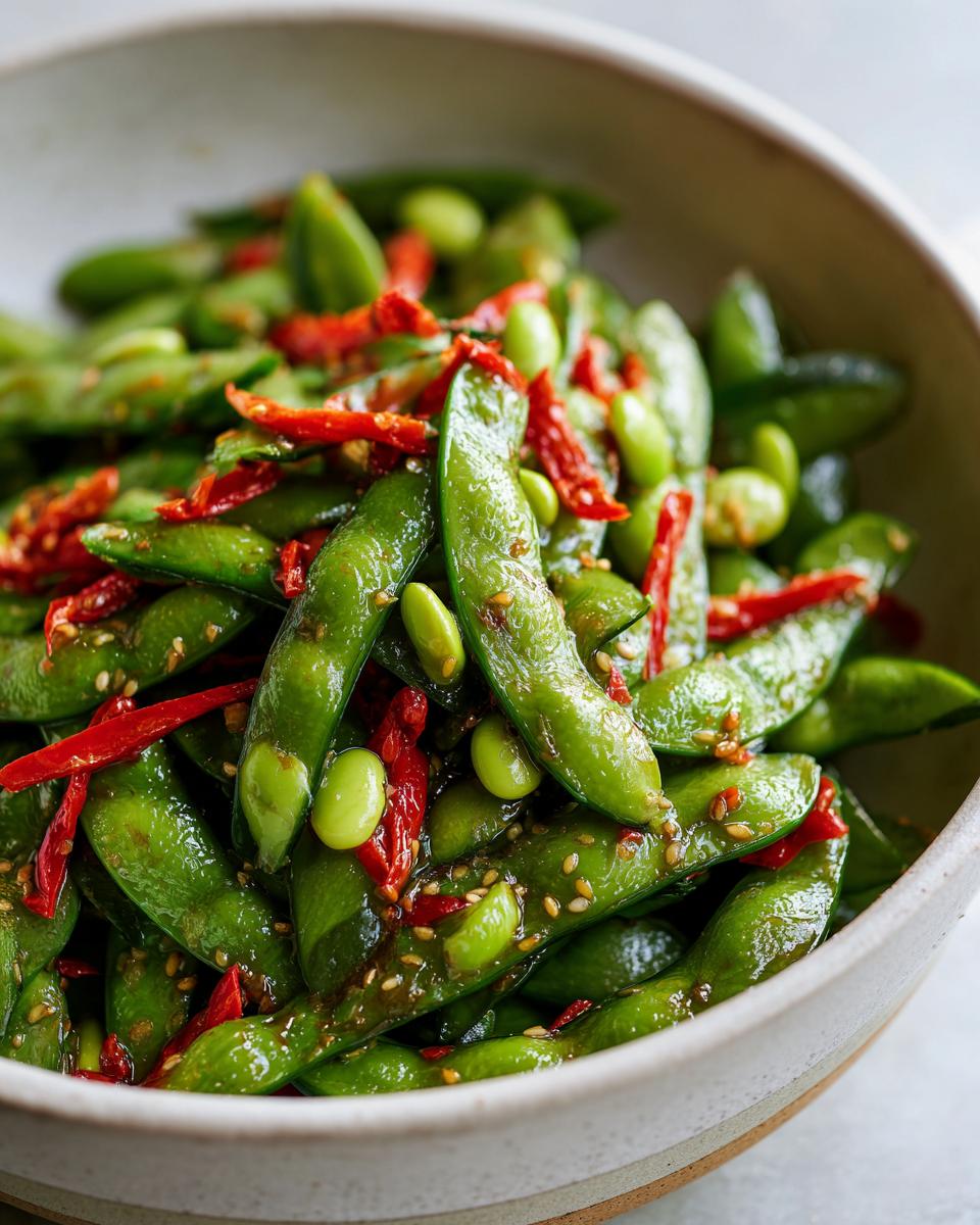 Close-up of bright green edamame pods tossed with red chili strips and sesame seeds, part of a cucumber edamame salad.