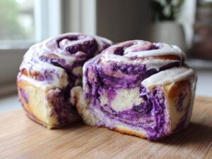 Two soft ube cinnamon rolls with vibrant purple swirls and white icing sitting on a wooden board.