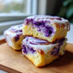 A stack of three soft ube cinnamon rolls, drizzled with white icing, showing the vibrant purple ube filling.