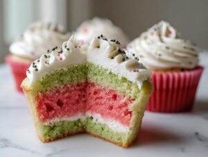 Close-up of a watermelon cupcakes cut in half showing pink, green, and white layers and white frosting with sprinkles.
