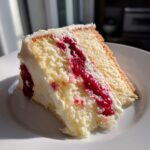 Close-up of a moist slice of white chocolate raspberry layer cake showing layers of white cake, thick white frosting, and bright red raspberry filling.