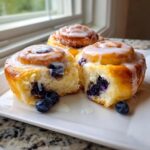 Close-up of three soft Blueberry Lemon Sweet Rolls drizzled with white icing, one roll pulled apart to show blueberries inside.