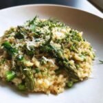 A close-up of creamy Asparagus Risotto topped with shaved Parmesan cheese and fresh dill.