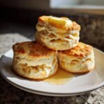 A stack of three fluffy Honey Butter Biscuits topped with melting butter and drizzled with honey.