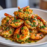 A close-up of perfectly cooked Garlic Butter Shrimp piled high on a white plate, glistening with butter sauce and fresh parsley.