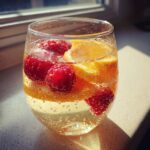 Close-up of a glass filled with bubbly Moscato Sangria, garnished with fresh raspberries and orange slices.