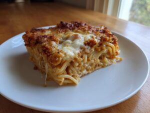 A square slice of baked leftover spaghetti bake with a crispy, cheesy top, served on a white plate.