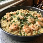 Close-up of creamy one pan shrimp orzo topped with fresh parsley and grated cheese in a dark skillet.