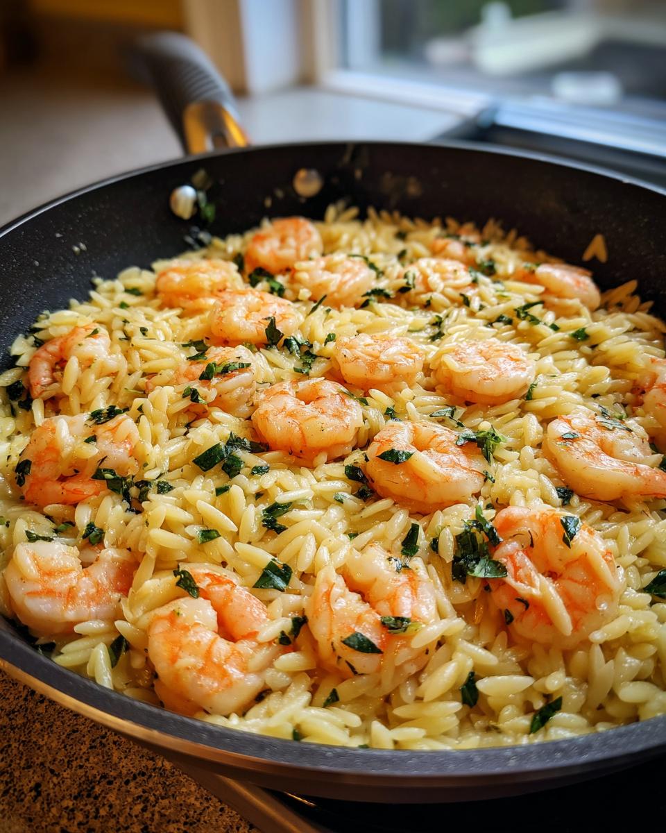 Close-up of creamy one pan shrimp orzo topped with cooked shrimp and fresh parsley in a black skillet.