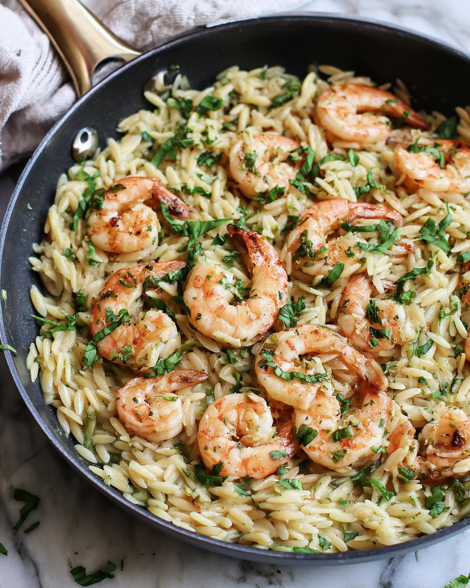 A close-up overhead view of juicy shrimp nestled in creamy orzo pasta, garnished with fresh parsley, ready to serve from the pan.