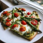 Close-up of two slices of Pesto pizza topped with melted mozzarella, roasted cherry tomatoes, and whole asparagus spears.