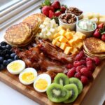 A beautiful, abundant breakfast grazing board featuring bacon, pancakes, cheese cubes, berries, and hard-boiled eggs.