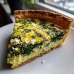 A close-up slice of savory Spinach quiche with visible feta cheese and a golden crust, served on a white plate.
