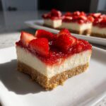 A single, thick slice of strawberry cheesecake bars showing a graham cracker crust, creamy filling, and topped with fresh strawberries.